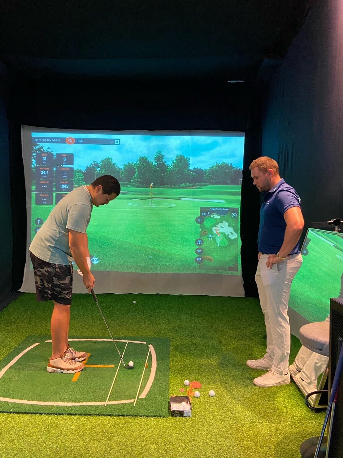 A golf professional coaching a student in the simulator
